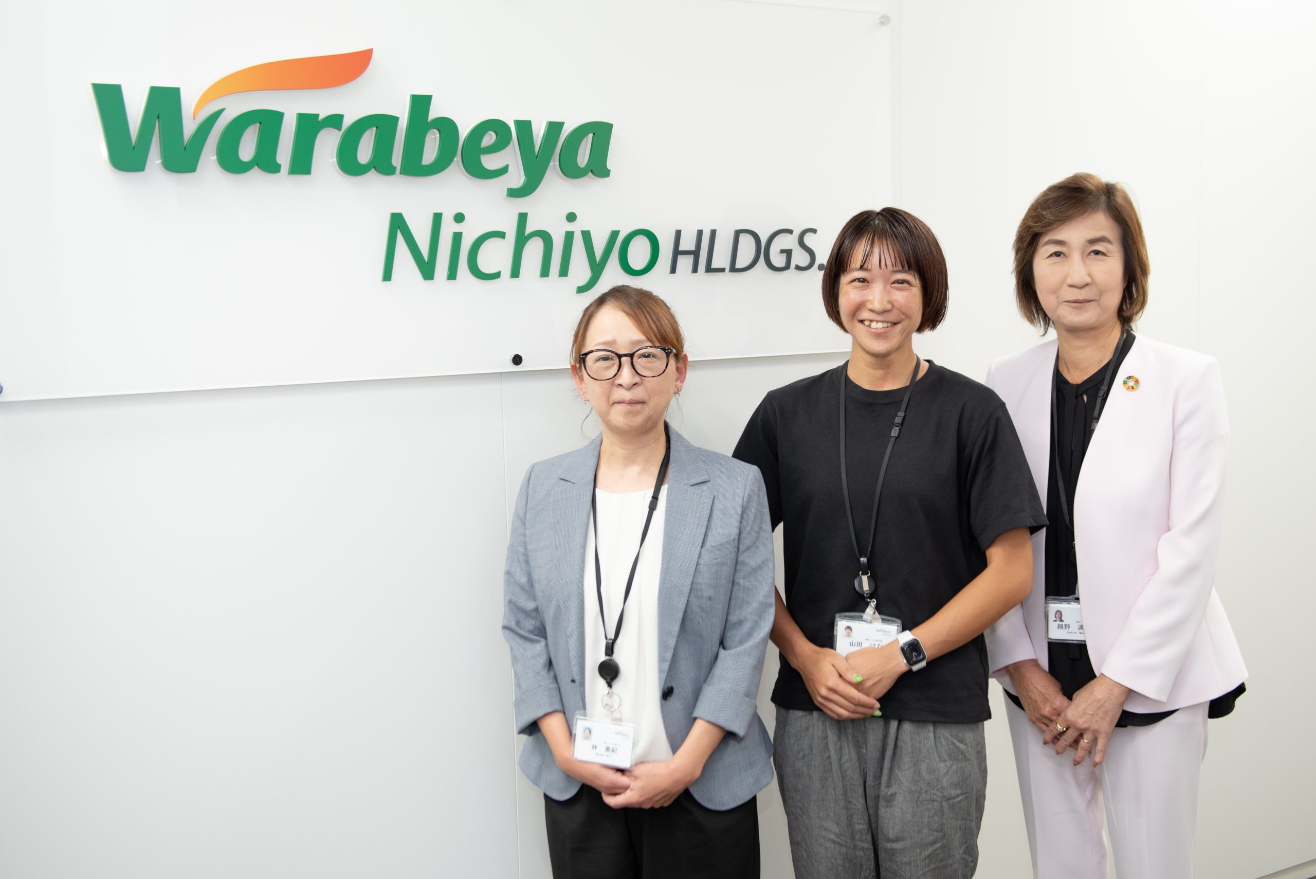 取材される3名が会社看板の前に立っている写真