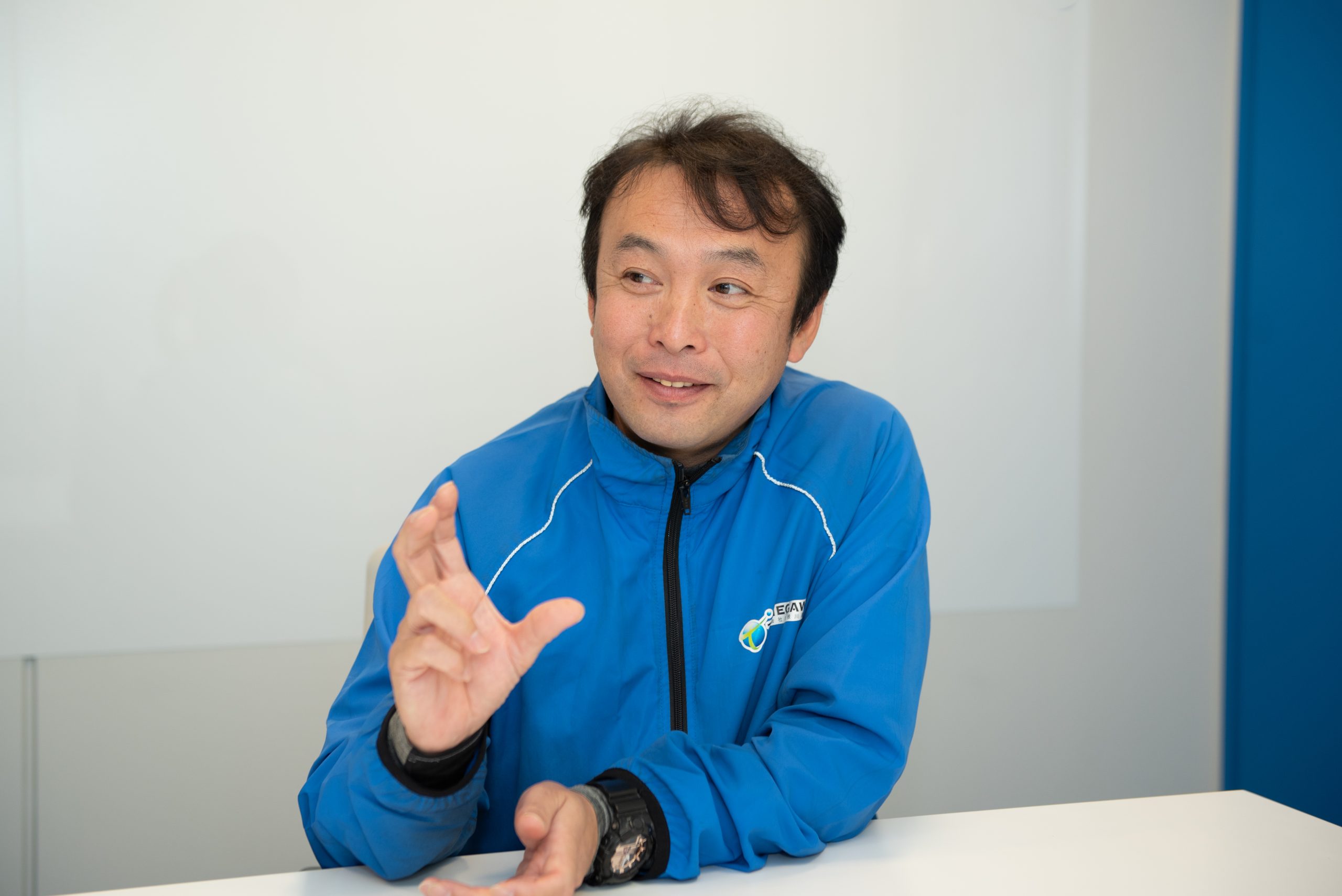 右手で何かのジェスチャーをしながらインタビューに応える塩屋さんの画像