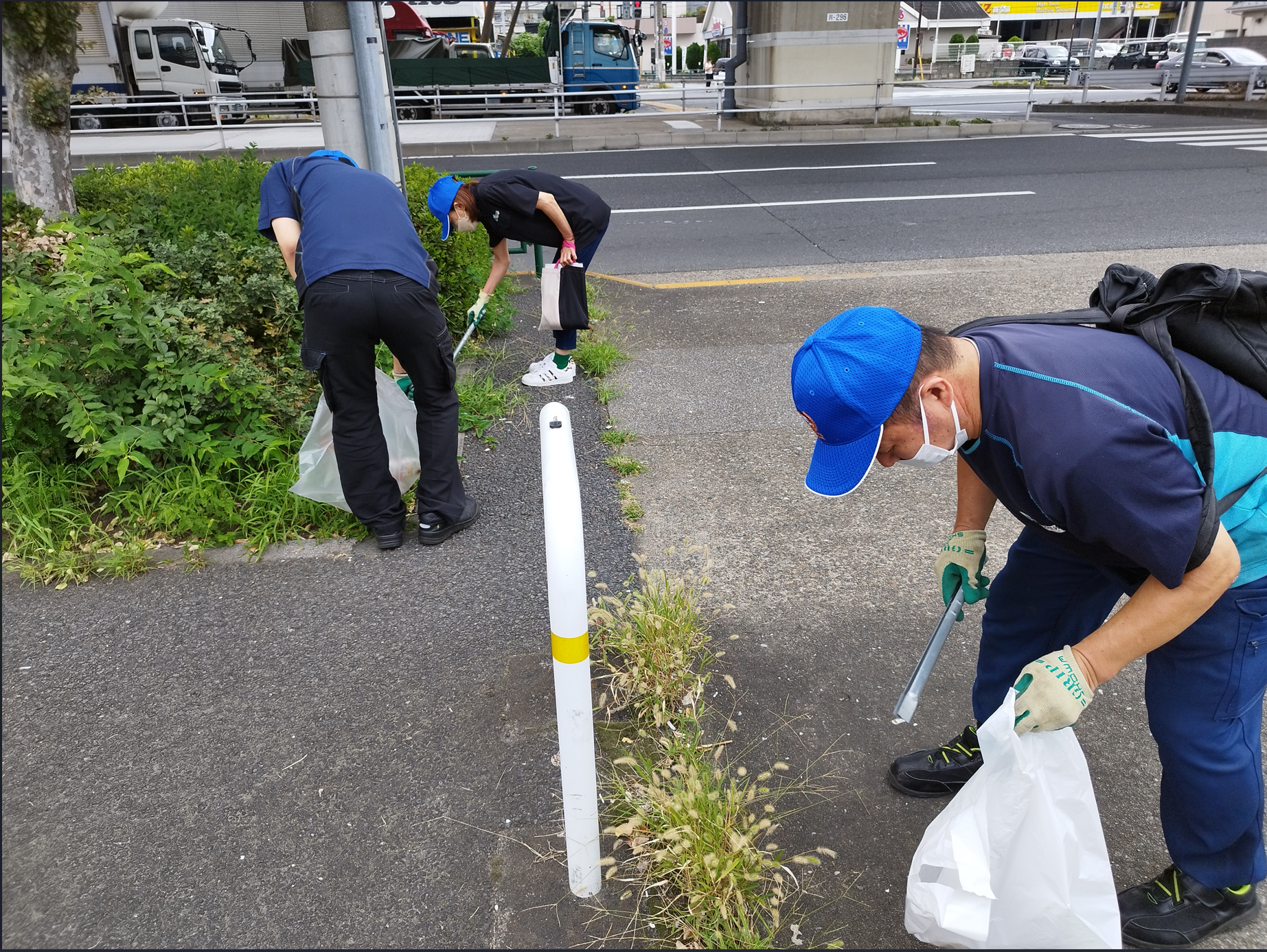 3名の社員が遠ろ脇のゴミをトングで拾っている写真