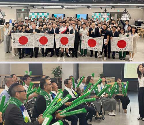 大勢の社員が国旗を持って選手と記念撮影している画像